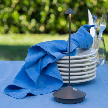 Pina Pro black die-cast aluminum LED lamp on a blue table with stacked white plates and a blue napkin.