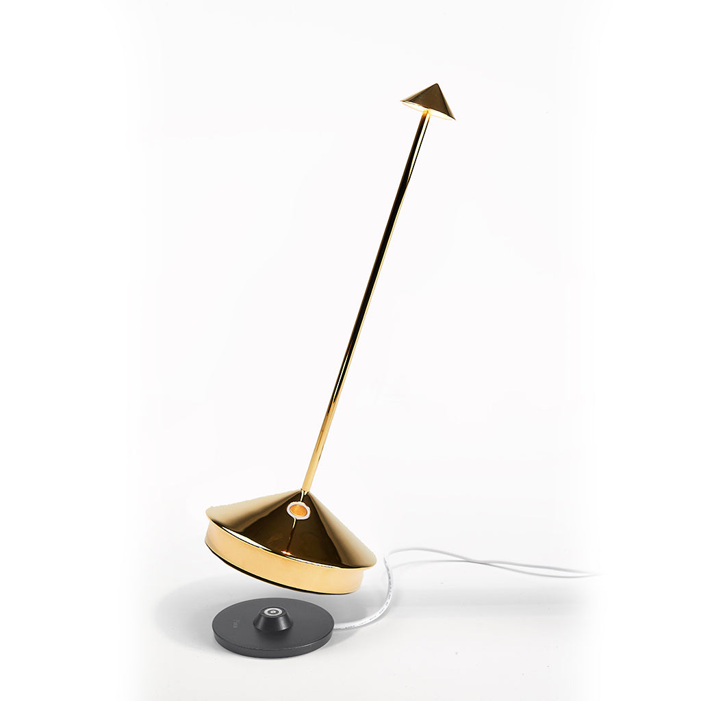 Pina Pro Glossy Gold rechargeable LED lamp with a broad base, thin rod, and small shade, on a charging pad.