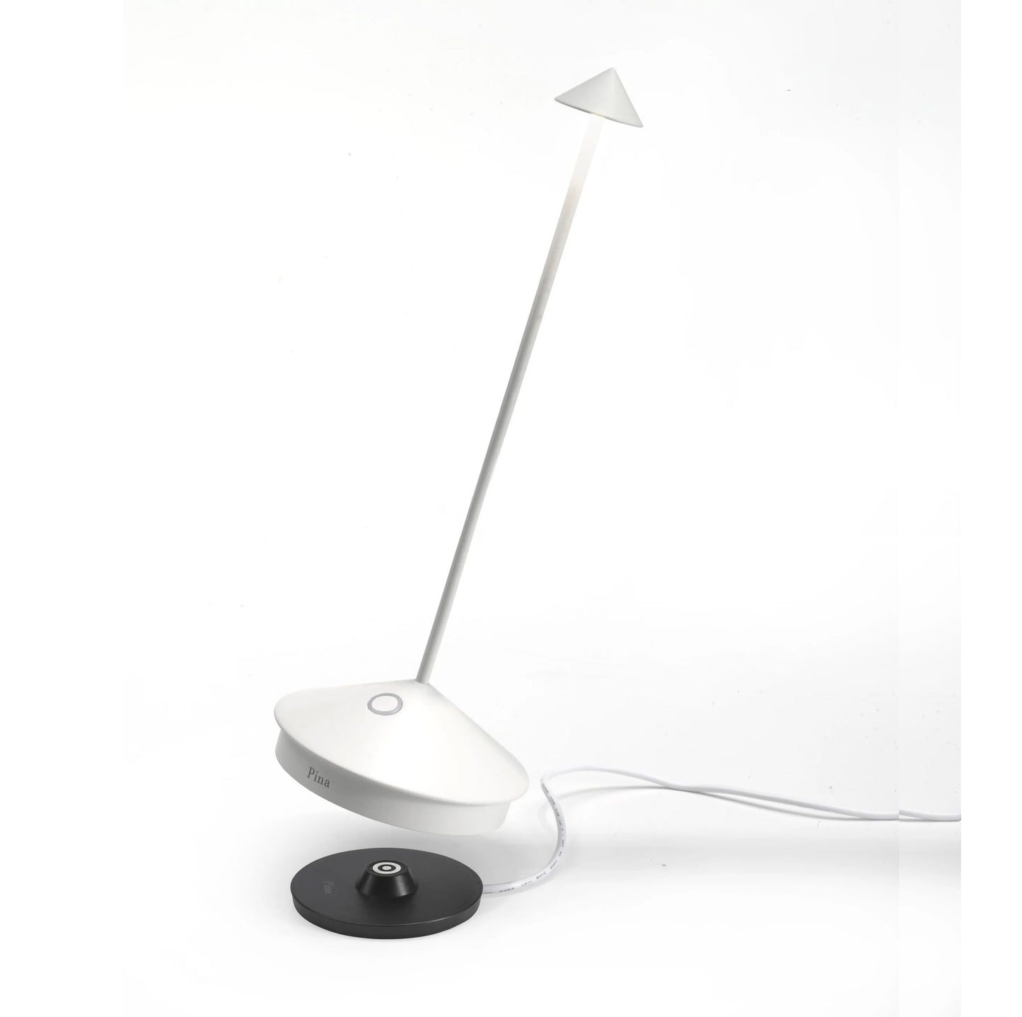 White Pina Pro rechargeable LED lamp with die-cast aluminum base, thin rod, and polycarbonate shade, next to a black charging base.
