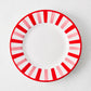 Round ceramic salad plate with a white center and a pink and red striped border on a light gray background.