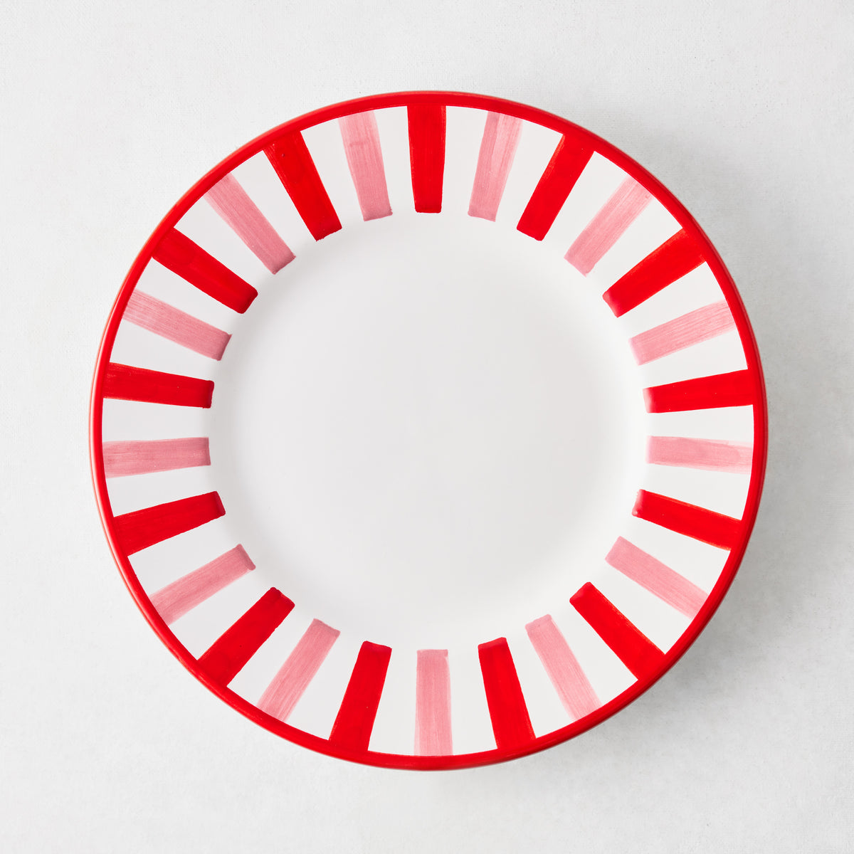 Round ceramic salad plate with a white center and a pink and red striped border on a light gray background.
