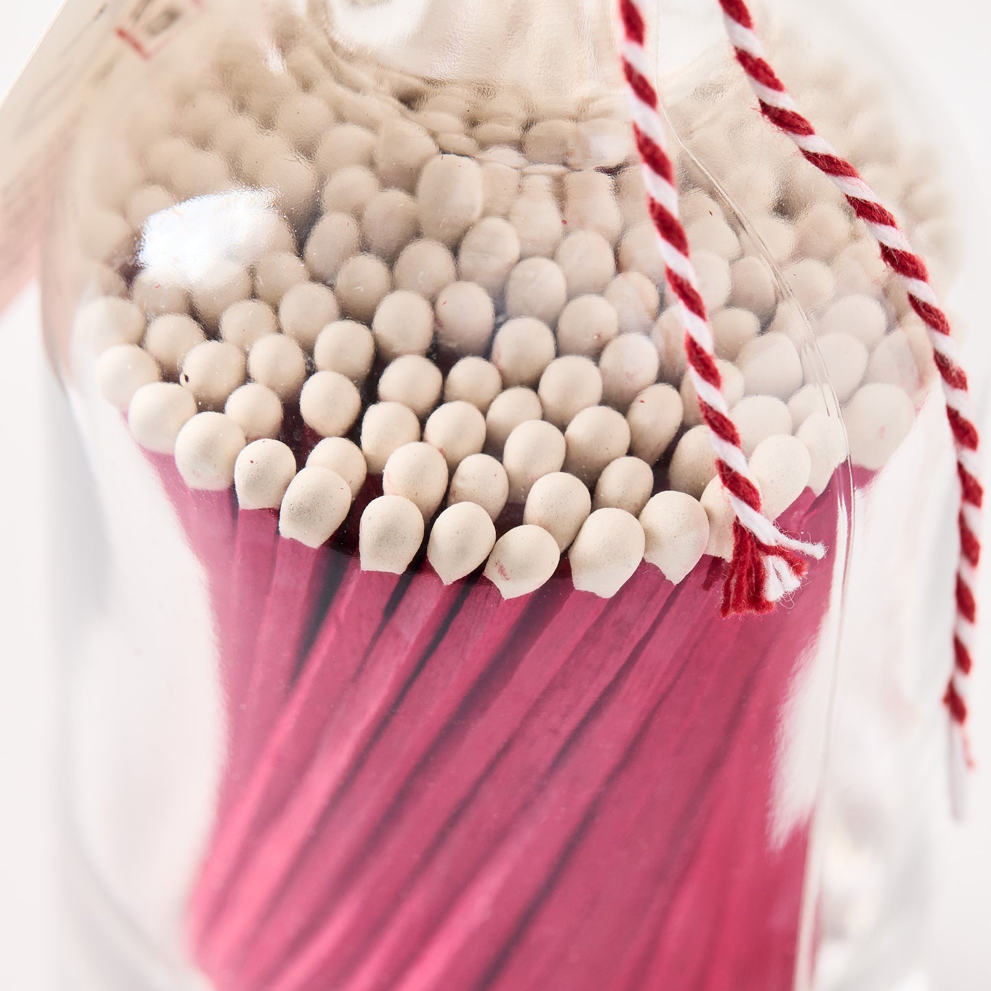 Pink with white tip oversized matches in a clear glass bottle with red and white twine.