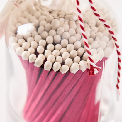 Pink with white tip oversized matches in a clear glass bottle with red and white twine.