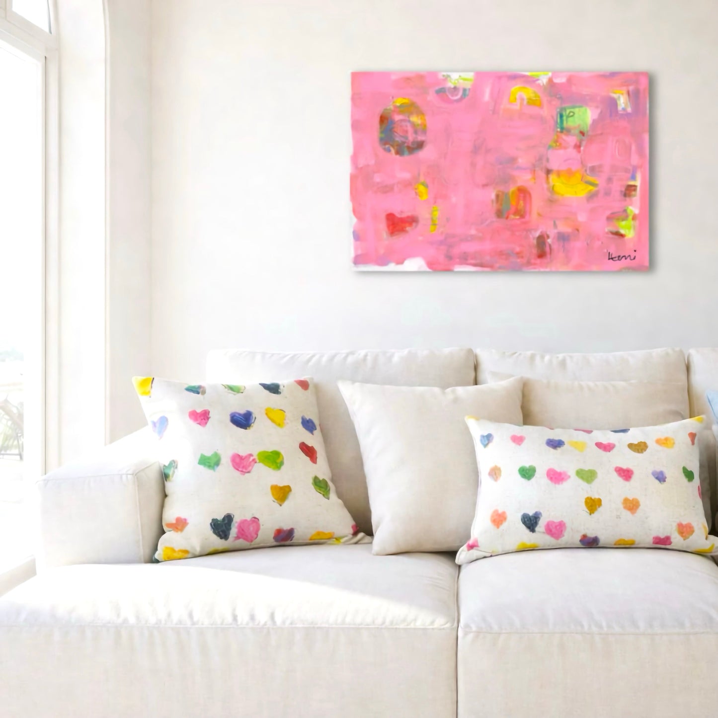 Kerri Rosenthal's "Pinkaholic" abstract art print, featuring vibrant pinks, yellows, and heart shapes, above a white sofa.
