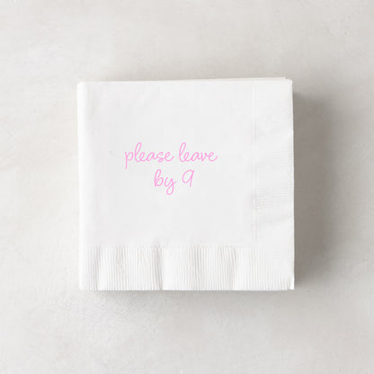 White 3-ply paper cocktail napkin with "please leave by 9" in pink script, 5.5" square.
