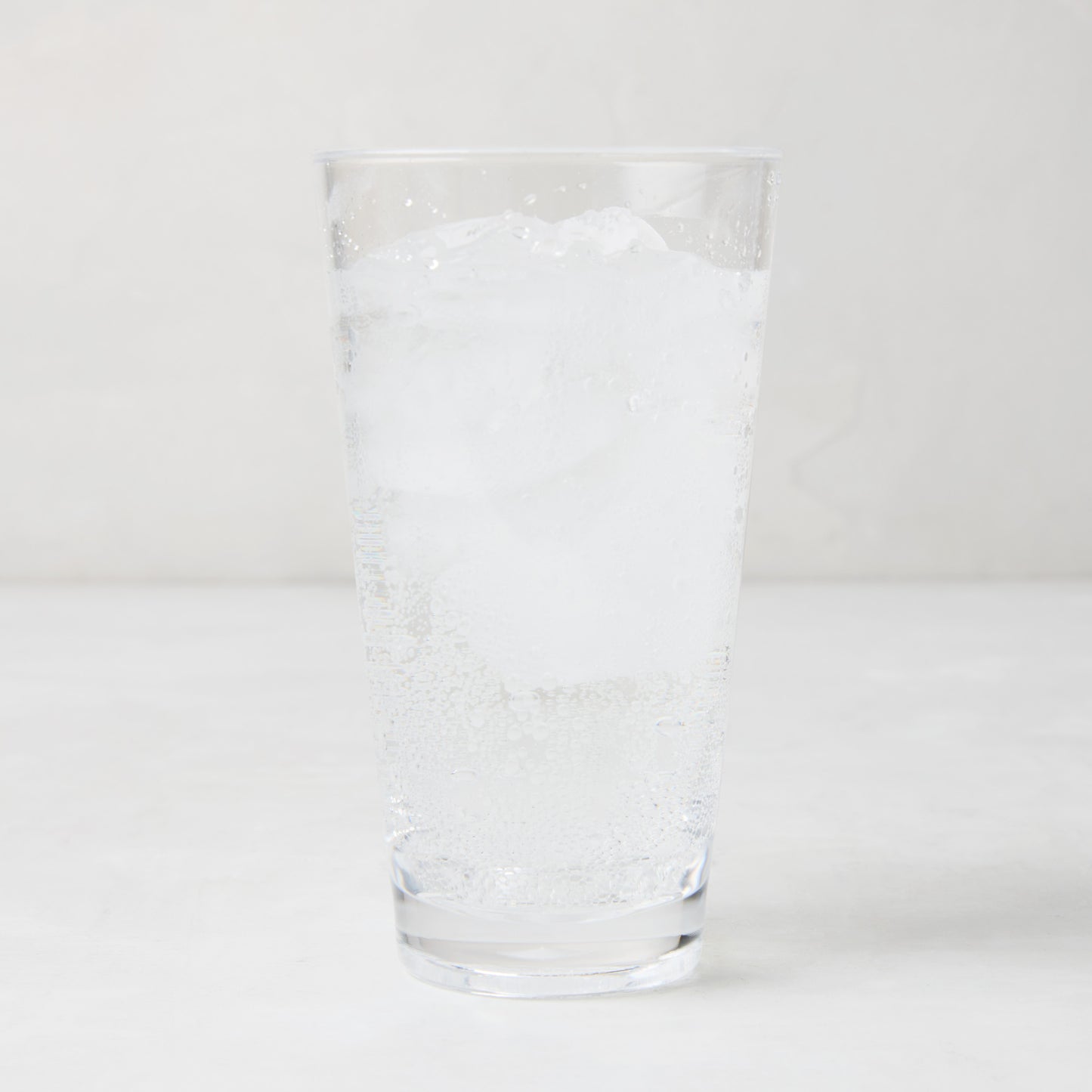 Clear acrylic highball glass with ice and sparkling water.