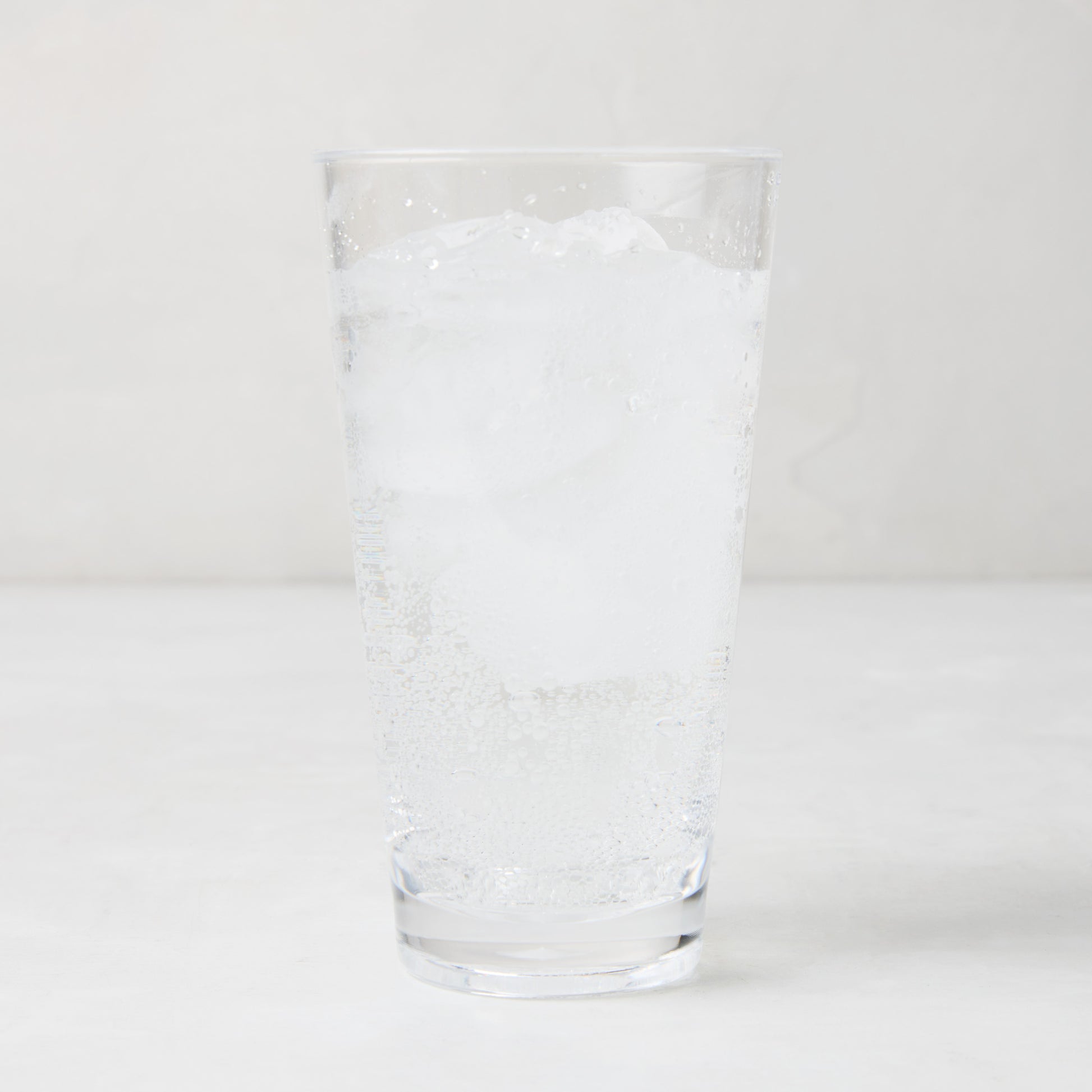Clear acrylic highball glass with ice and sparkling water.