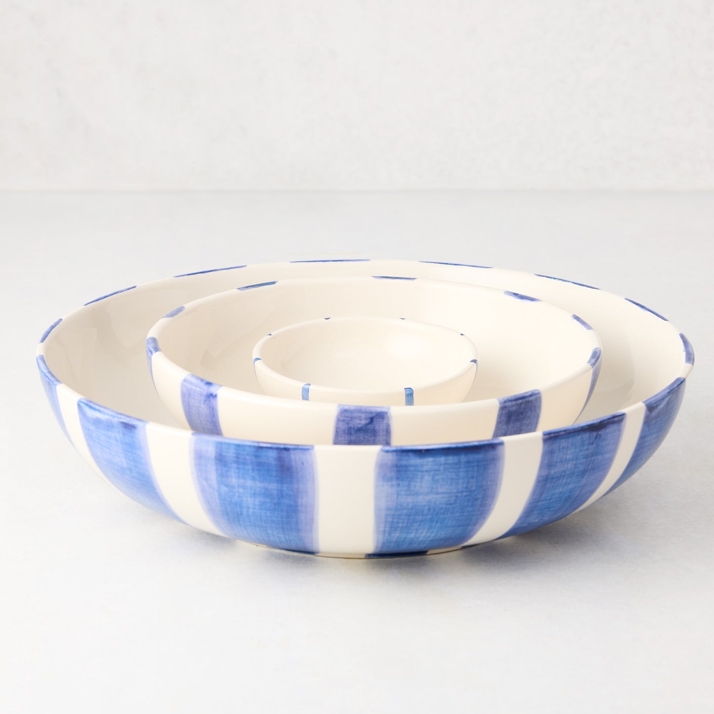 Three nested Portofino blue stripe ceramic serve bowls, large to small.