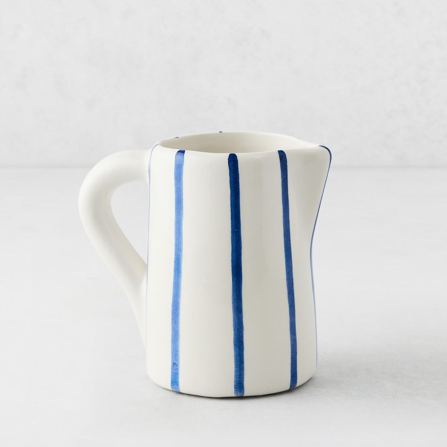 Small Portofino ceramic pitcher with white glaze, hand-painted blue vertical stripes, curved handle, and spout.