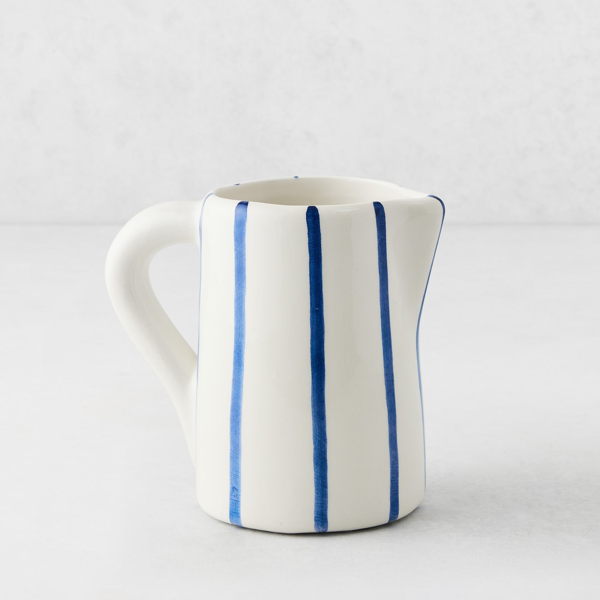 Small Portofino ceramic pitcher with white glaze, hand-painted blue vertical stripes, curved handle, and spout.