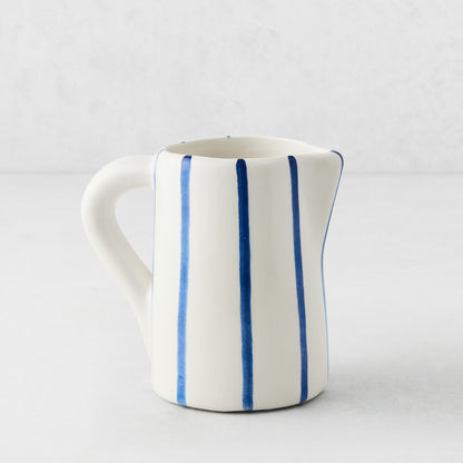 Small Portofino ceramic pitcher with white glaze, hand-painted blue vertical stripes, curved handle, and spout.