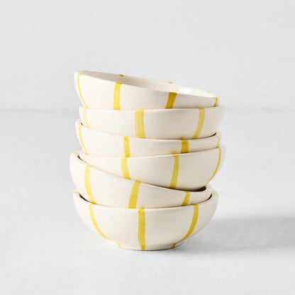Stacked Portofino ceramic dipping bowls, off-white with hand-painted yellow vertical stripes.