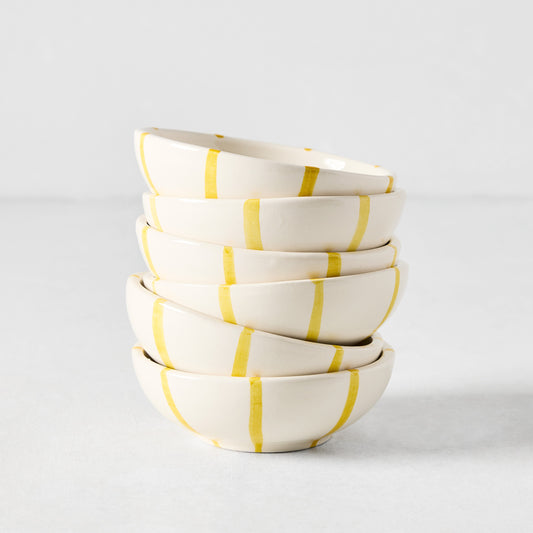 Stacked Portofino ceramic dipping bowls, off-white with hand-painted yellow vertical stripes.