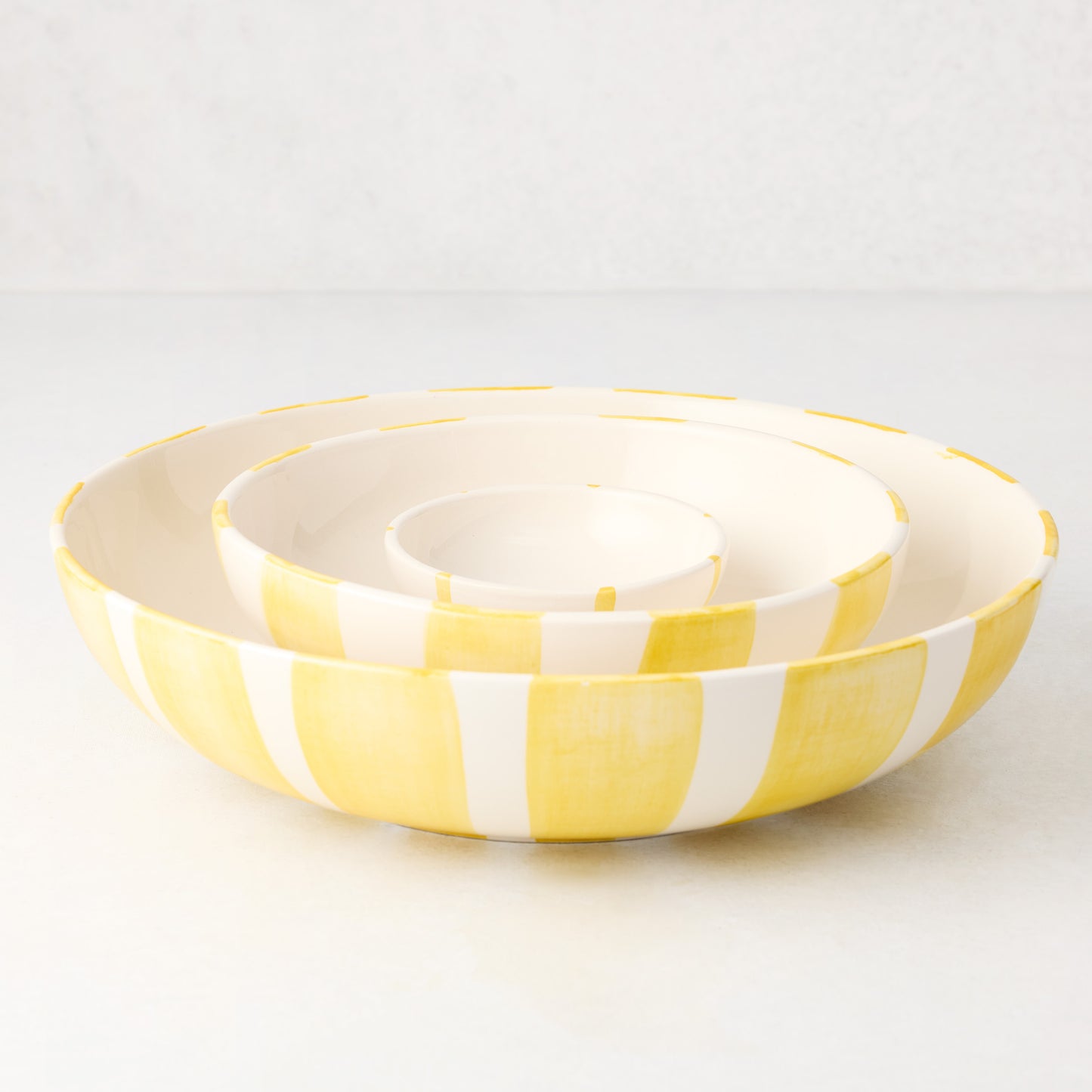 Three nested Portofino ceramic serve bowls with hand-painted yellow stripes.