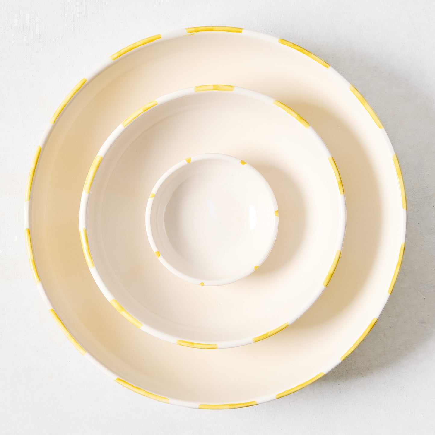 Three Portofino ceramic serve bowls, nested, with hand-painted yellow stripes on a cream background.