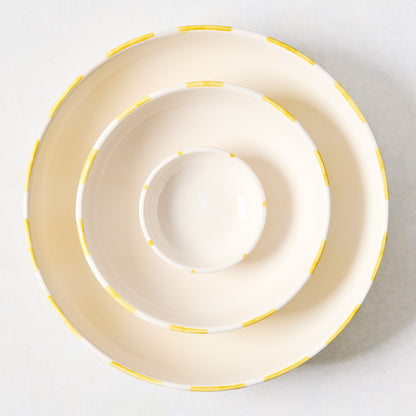 Three Portofino ceramic serve bowls, nested, with hand-painted yellow stripes on a cream background.