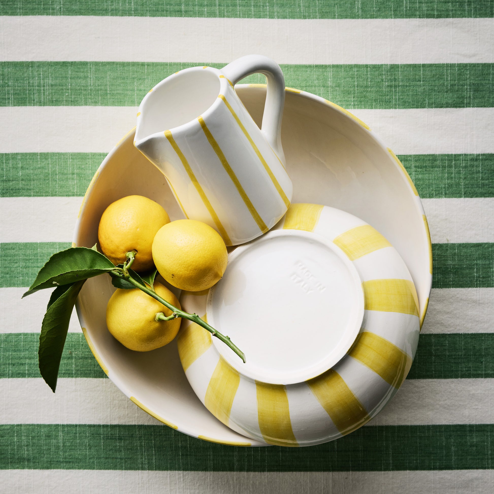 Portofino Yellow Stripe Large Ceramic Serve Bowl with pitcher, plate, and lemons on a green striped tablecloth.