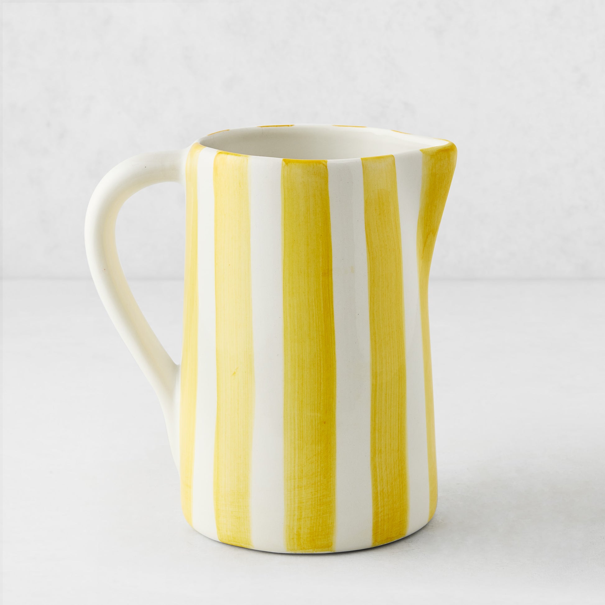 Medium Portofino ceramic pitcher with hand-painted yellow and white vertical stripes, curved handle and spout.