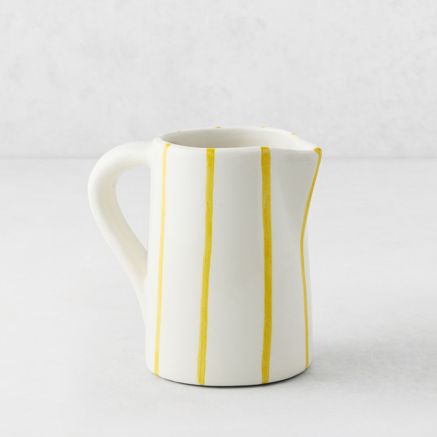 Small Portofino ceramic pitcher with white glaze and hand-painted thin yellow vertical stripes, curved handle and spout.
