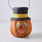 Vintage-style papier-mâché pumpkin candy bucket wearing a black top hat with a yellow band and wire handle.