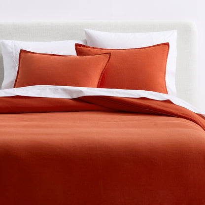 Pumpkin orange European washed linen duvet cover and matching shams layered with white bedding on a bed.