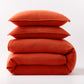Stacked pumpkin orange European washed linen duvet and two matching pillow shams on a white background.