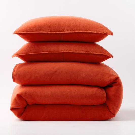Stacked pumpkin orange European washed linen duvet and two matching pillow shams on a white background.