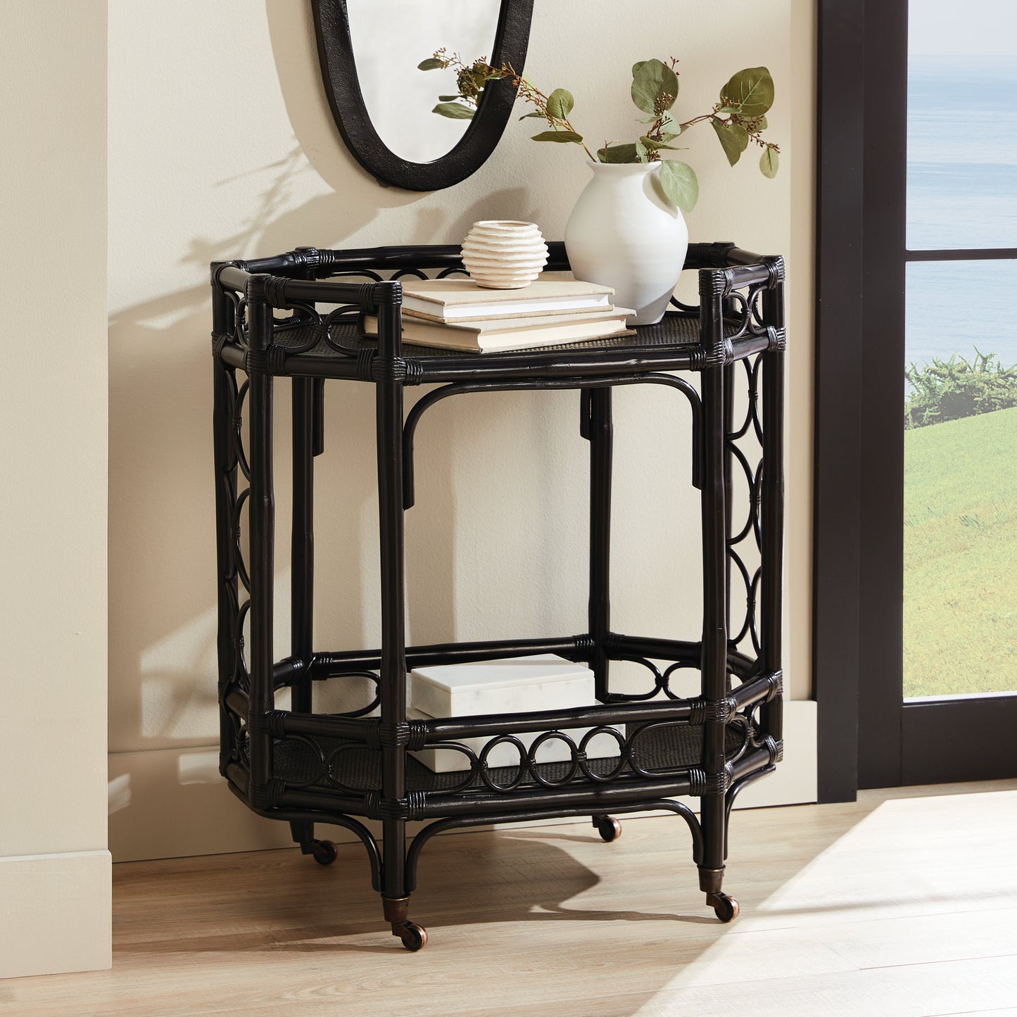 Raelyn black rattan bar cart with two shelves, dark wood, and casters.