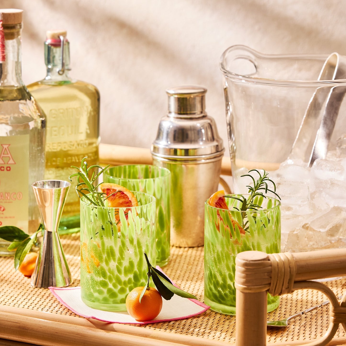Close-up of a Raelyn Bar Cart in natural rattan, holding cocktails, tequila bottles, and bar tools.