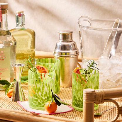 Close-up of a Raelyn Bar Cart in natural rattan, holding cocktails, tequila bottles, and bar tools.