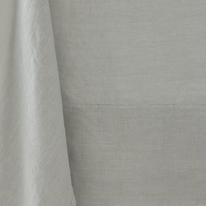 Hand-dyed grey linen tablecloth with visible fabric texture and a stitched border detail.