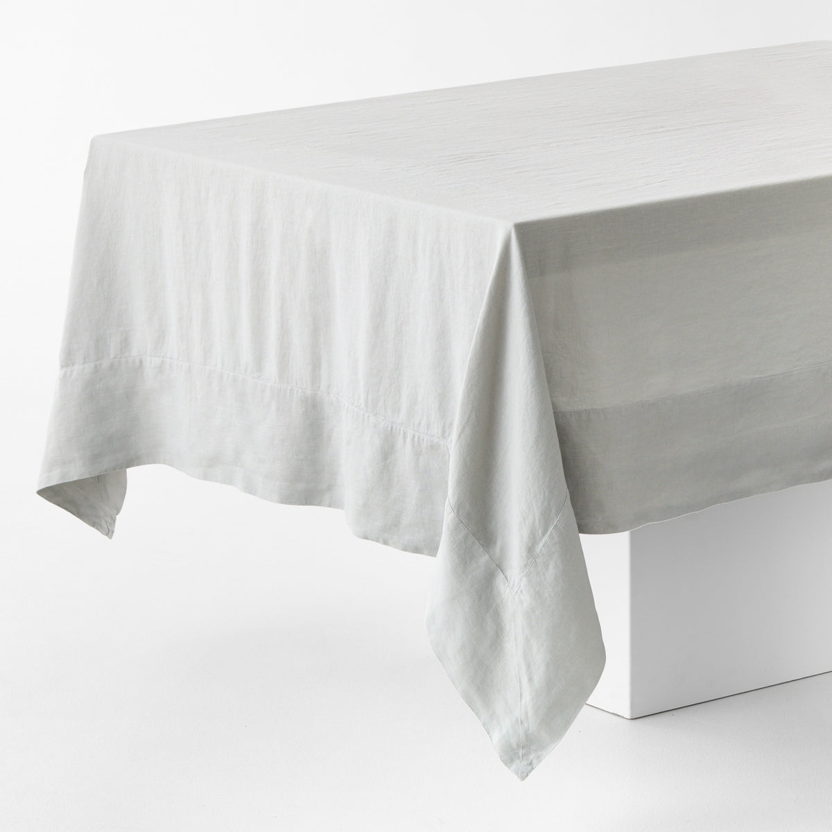 Light grey hand-dyed 100% linen tablecloth with mitered corner detailing on a white table.