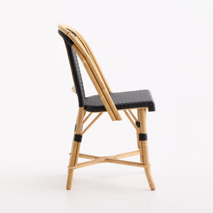 Side view of a French bistro chair with a natural rattan frame and black woven seat and backrest.