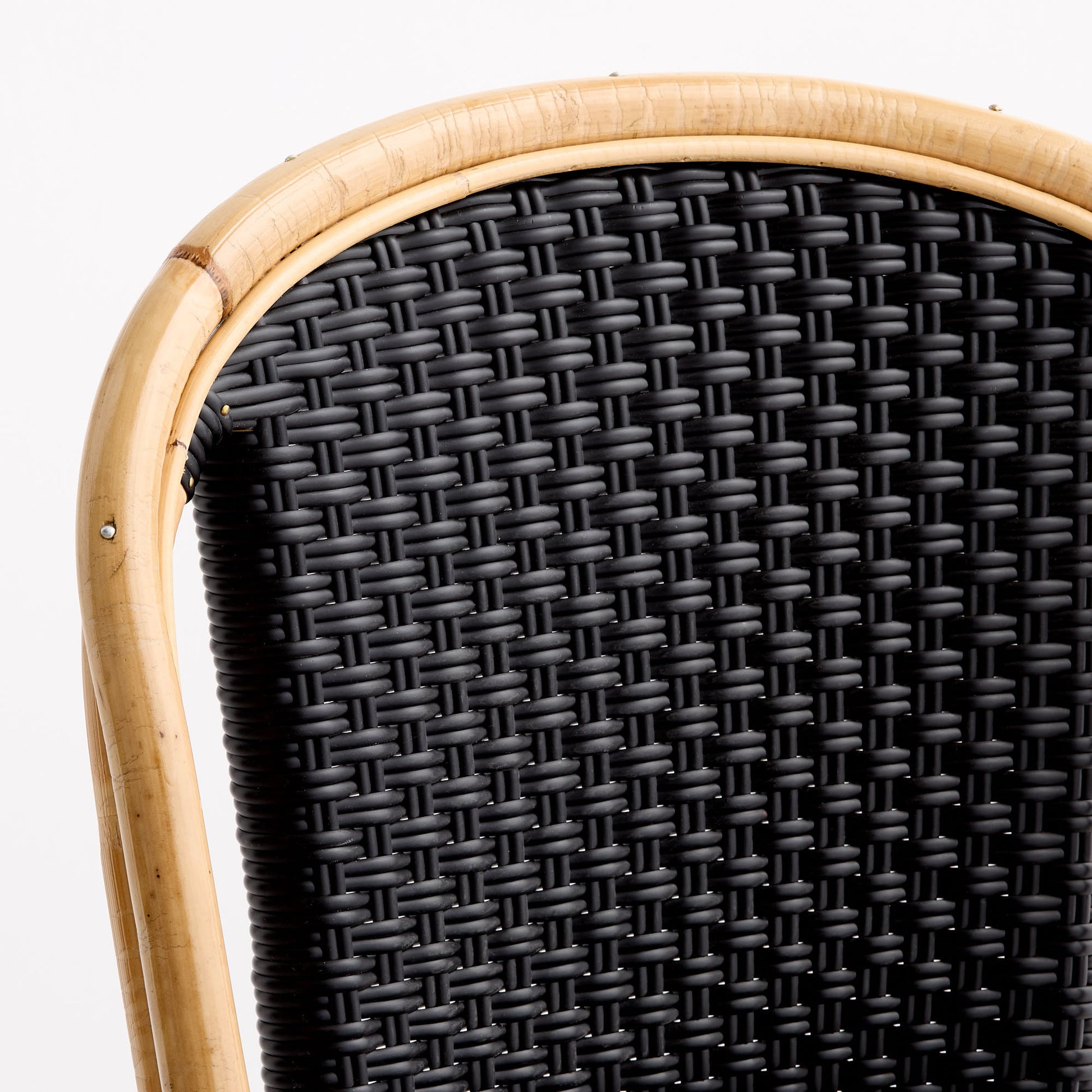 Close-up of a French bistro chair with a natural rattan frame and black woven rattan backrest.