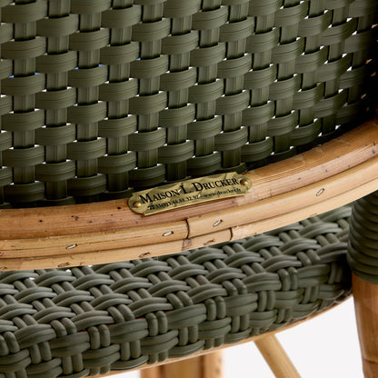 Olive green woven rattan bistro chair with a natural wooden frame and Maison L. Drucker brass nameplate.