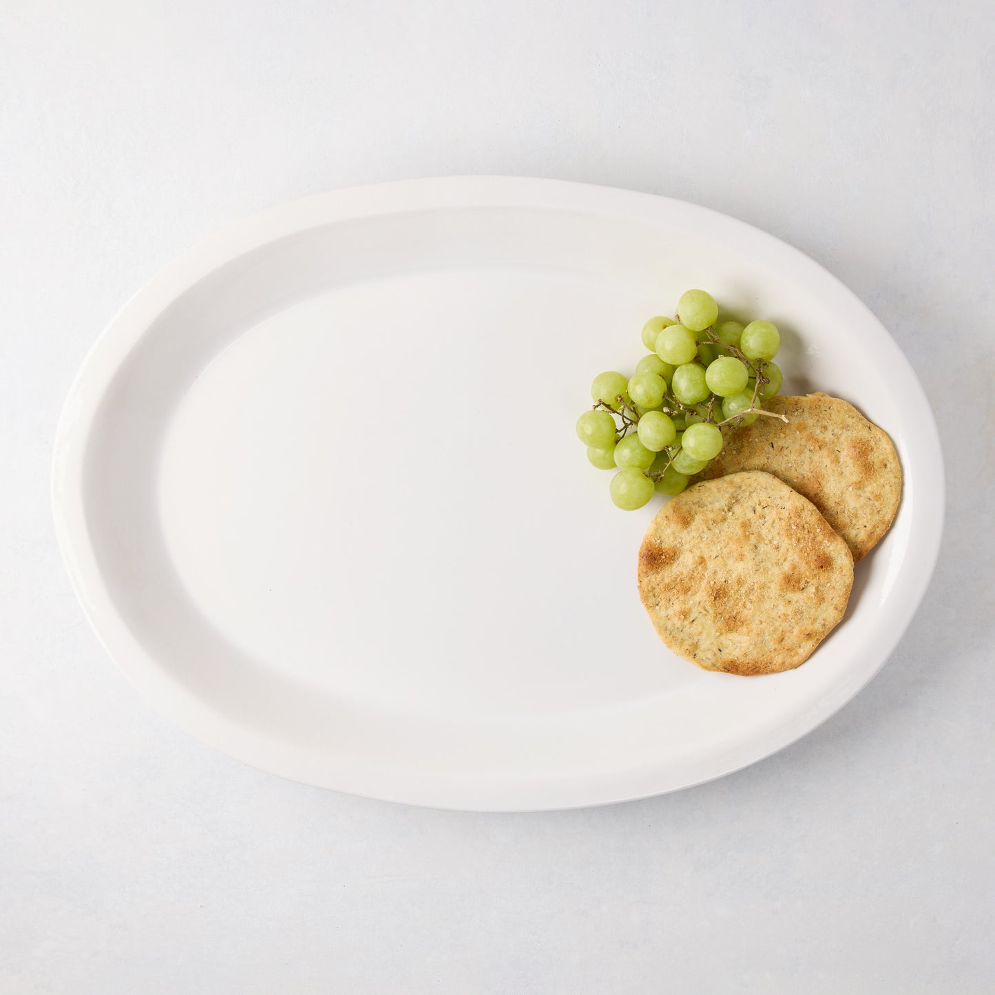 White Ravello Large Oval Stoneware Serving Platter with raised edge, holding grapes and crackers.