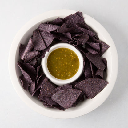 White Ravello stoneware chip and dip platter with built-in bowl, filled with blue chips and green salsa.