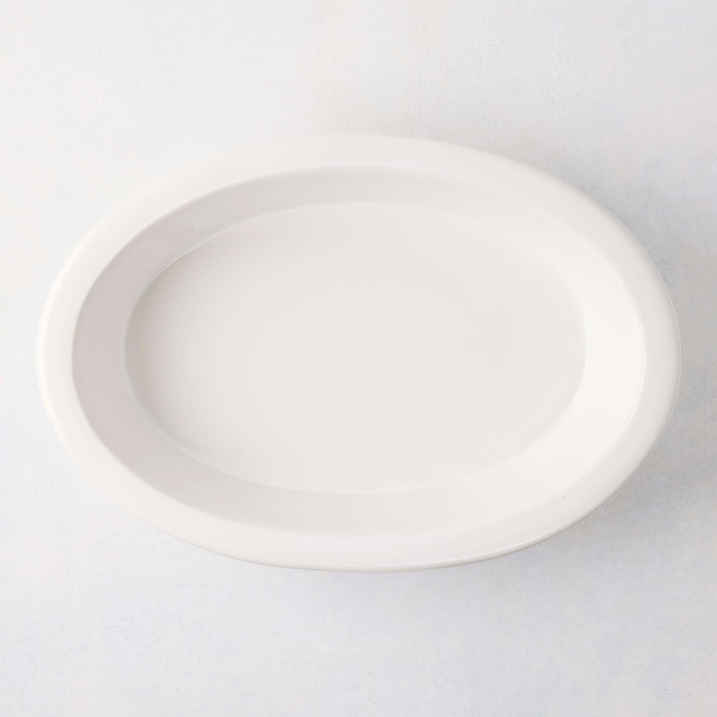 White Ravello Stoneware Oval Baking Dish, 13.6"L x 9.25"W, with an oversized lip.