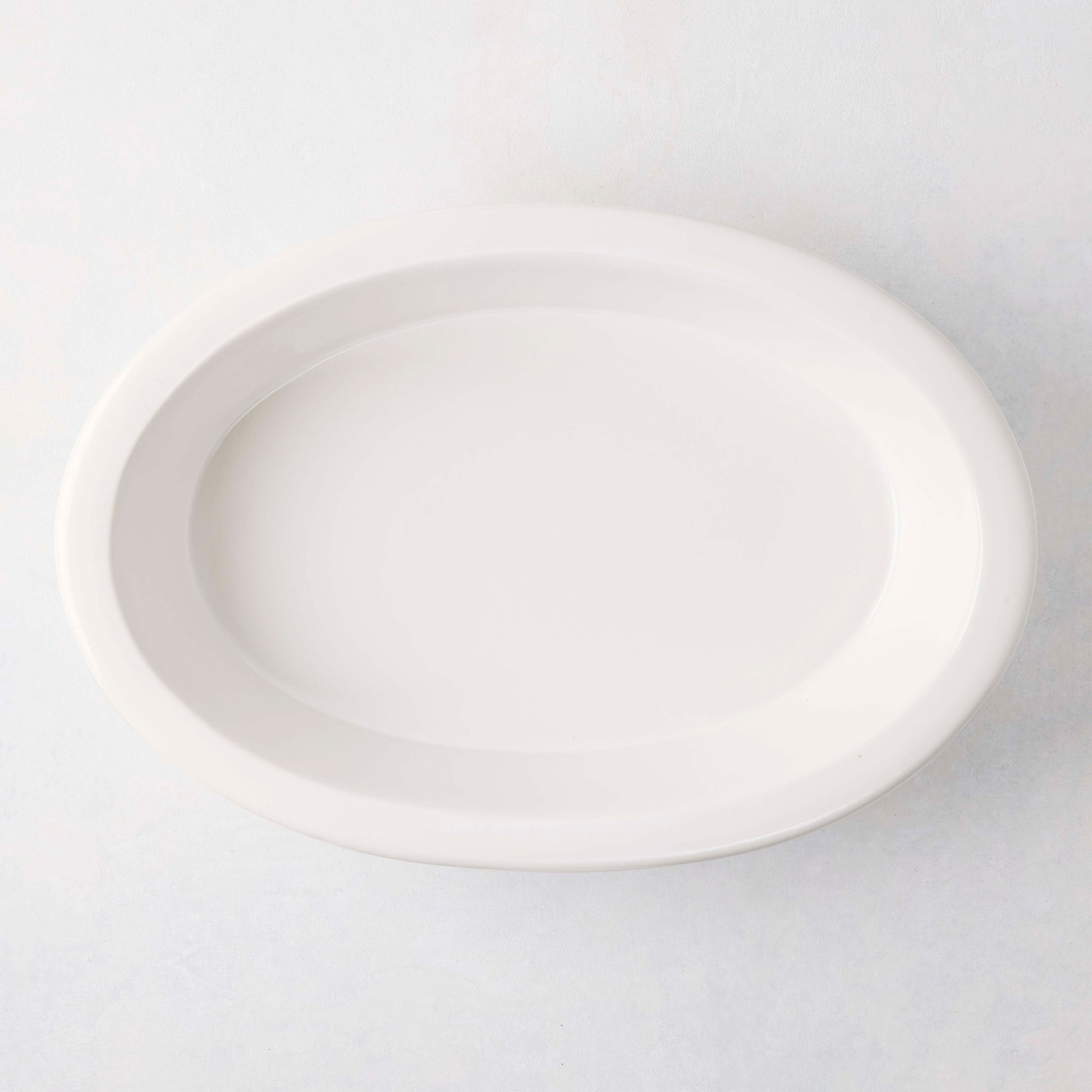 White Ravello Stoneware Oval Baking Dish, 13.6"L x 9.25"W, with an oversized lip.