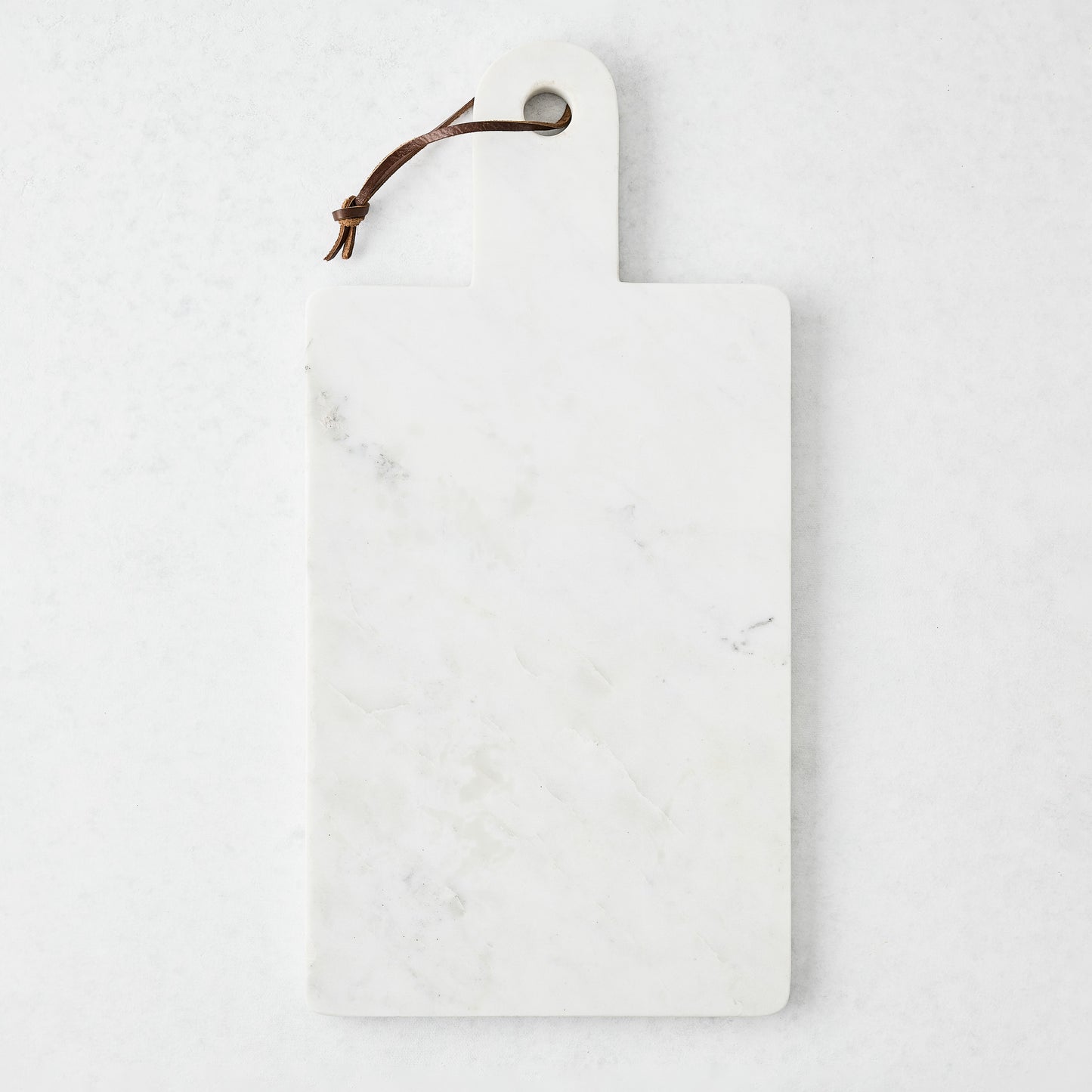 Rectangular white marble serve board with a sleek handle and brown leather strap.