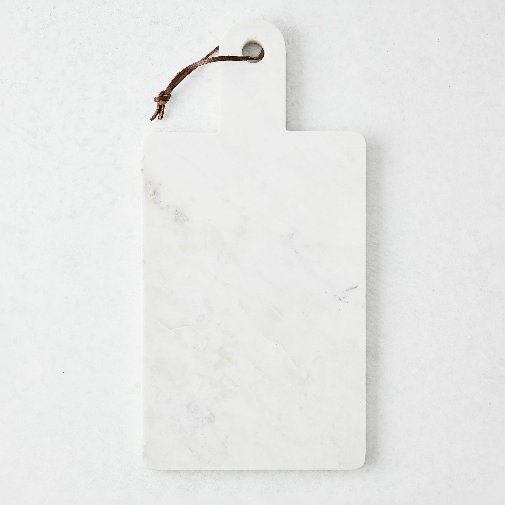 Rectangular white marble serve board with a sleek handle and brown leather strap.