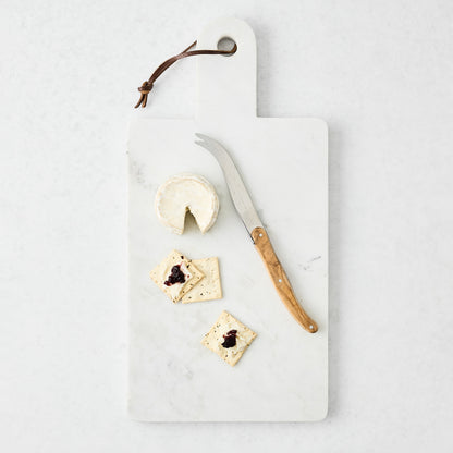 White rectangular marble serve board with handle, leather strap, cheese, crackers, and knife.