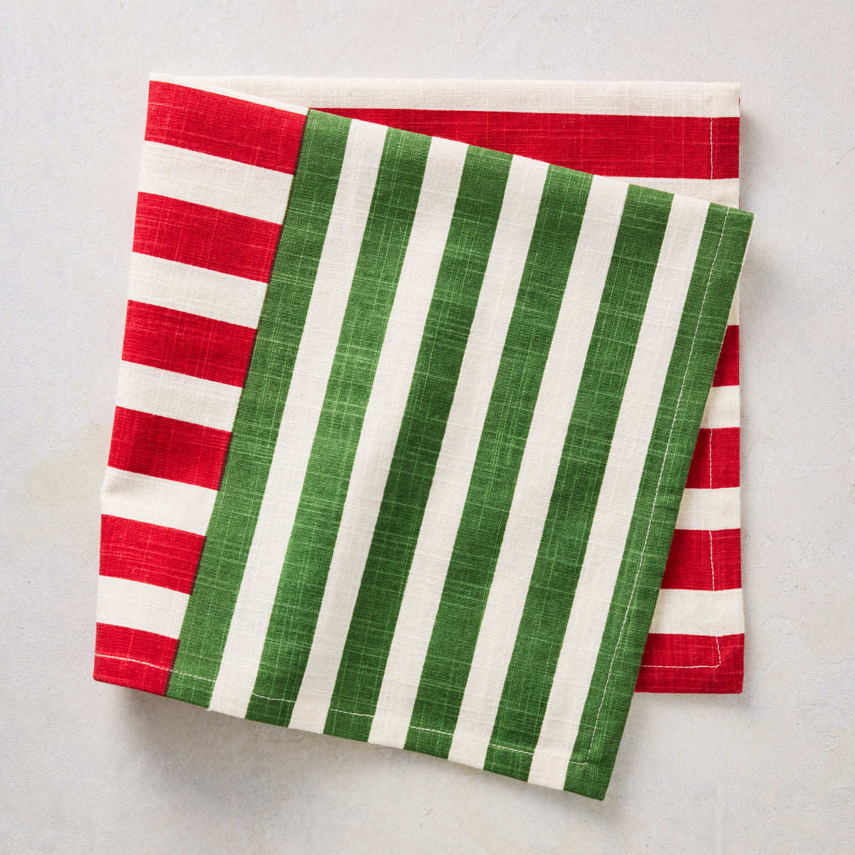 Folded cloth napkin with red and green vertical stripes on a cream background, featuring a modern holiday design.