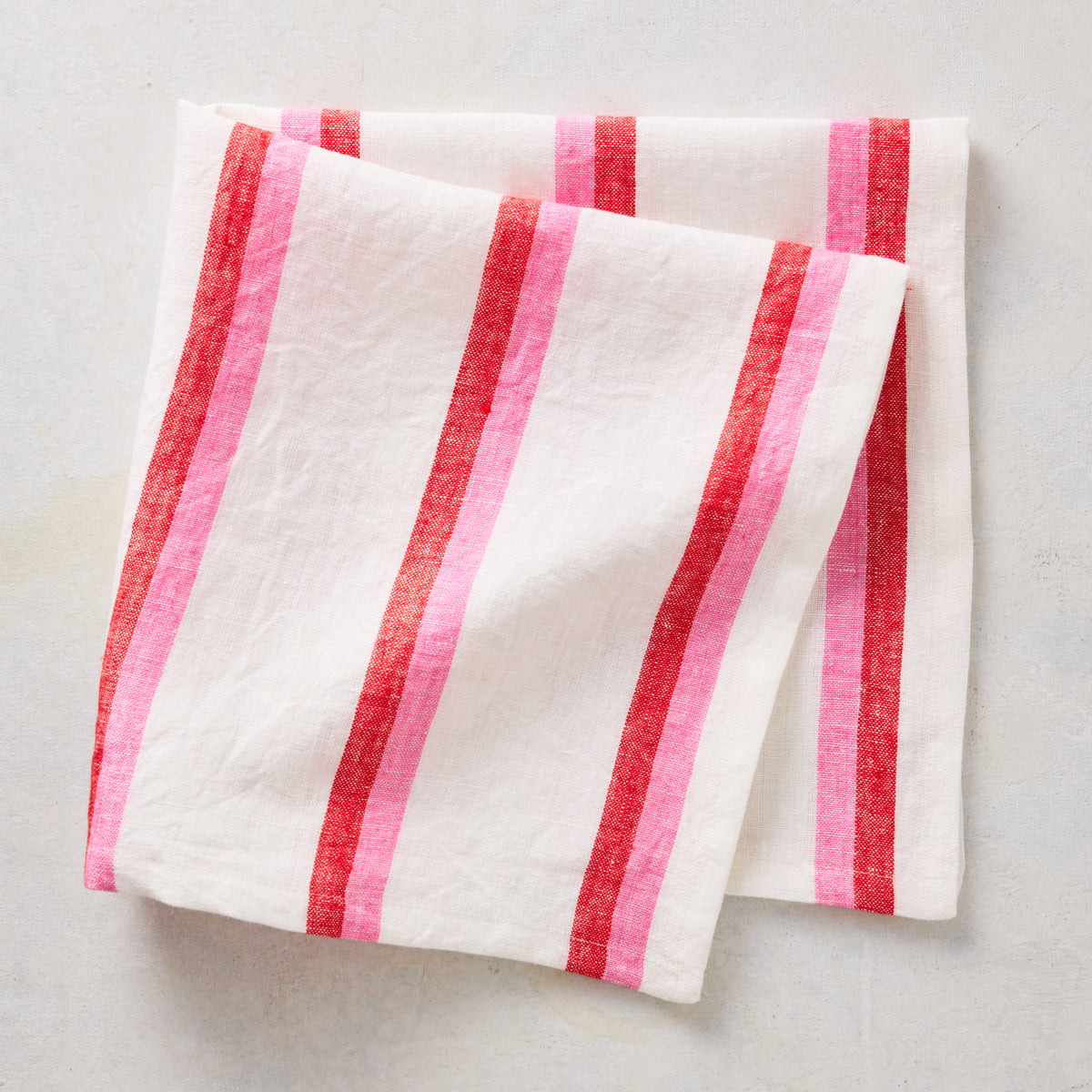 Folded linen napkin with red and pink candy cane stripes on a white background.