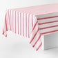 Rectangular tablecloth with red and pink candy cane stripes on a white linen-textured fabric draped over a table.