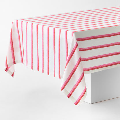 Rectangular tablecloth with red and pink candy cane stripes on a white linen-textured fabric draped over a table.