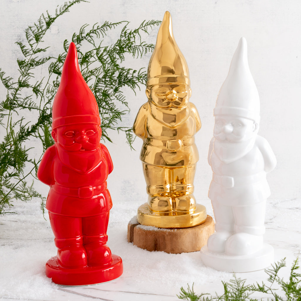 Red, gold, and white ceramic holiday gnomes on faux snow with green foliage.