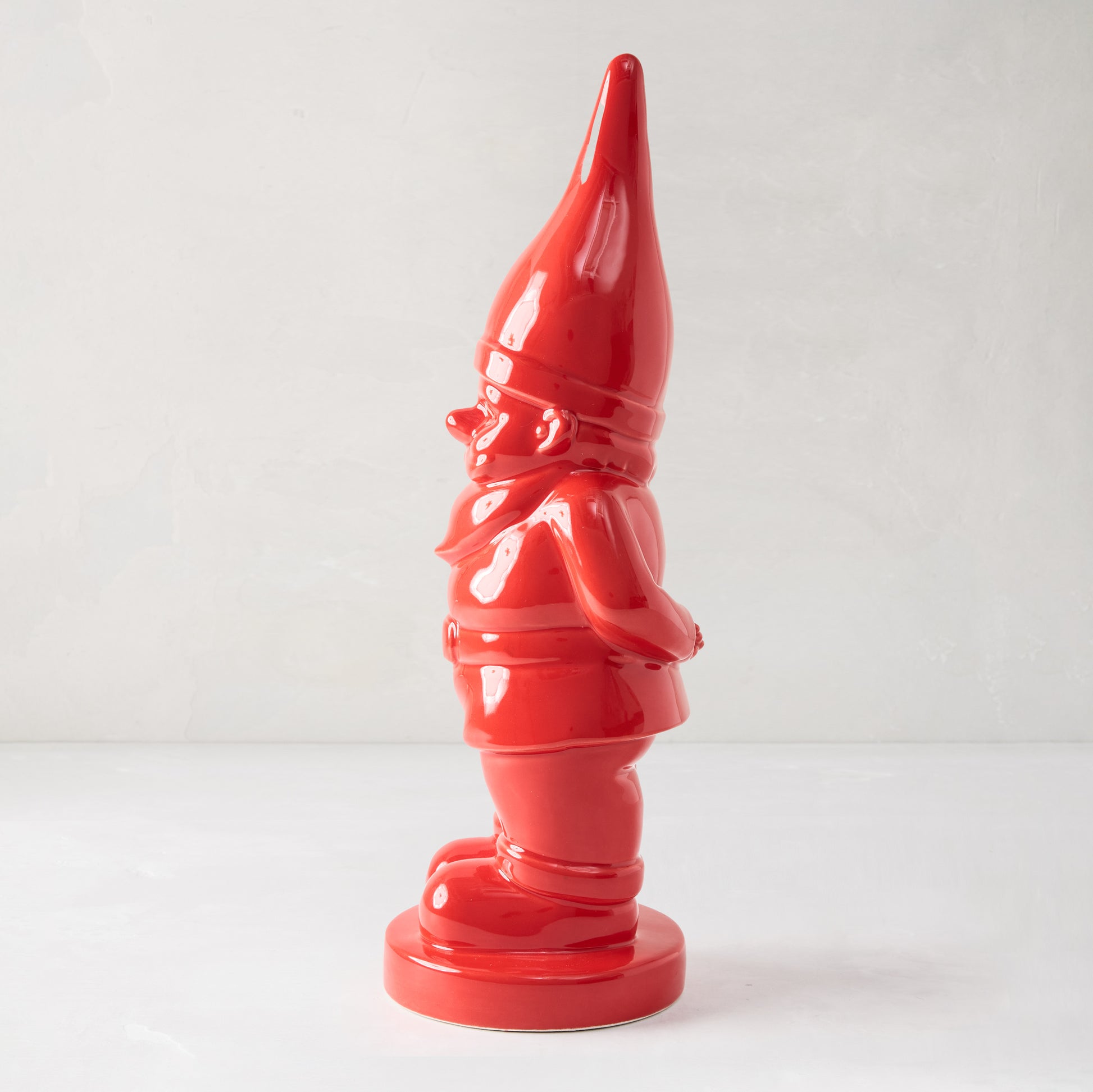 Tall, glossy red ceramic holiday gnome with pointed hat, standing on a round base.
