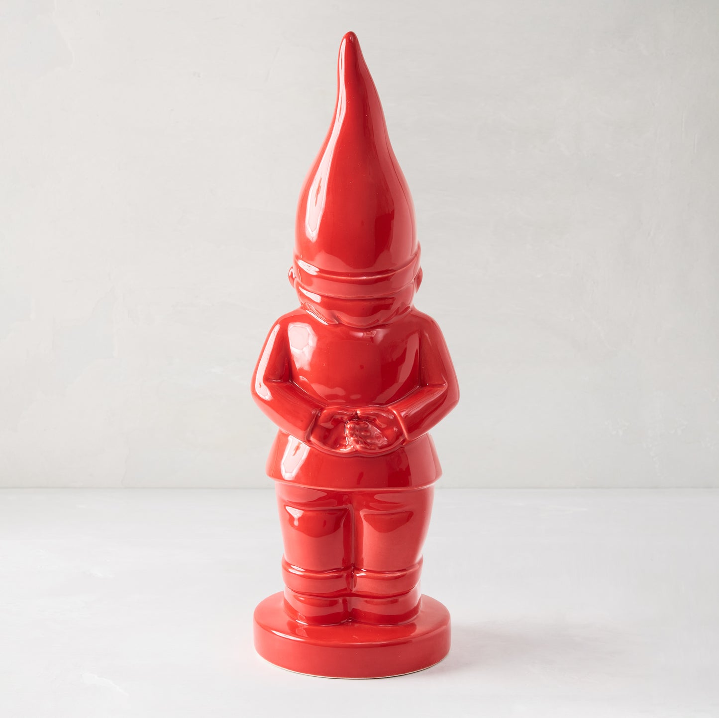 Red ceramic holiday gnome with a tall pointed hat, hands clasped, and a brilliant red glaze.