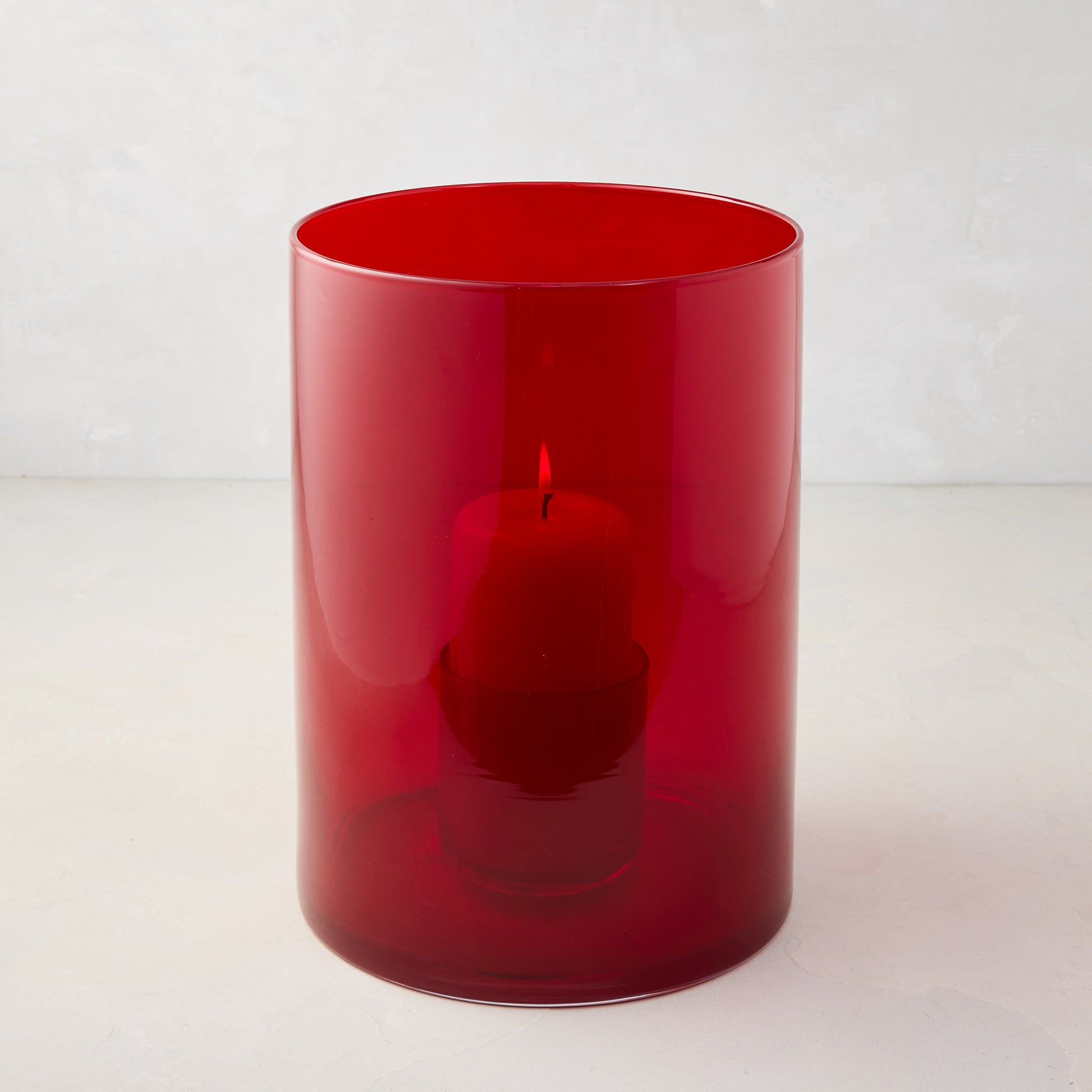 Medium red glass hurricane with a lit red pillar candle inside.